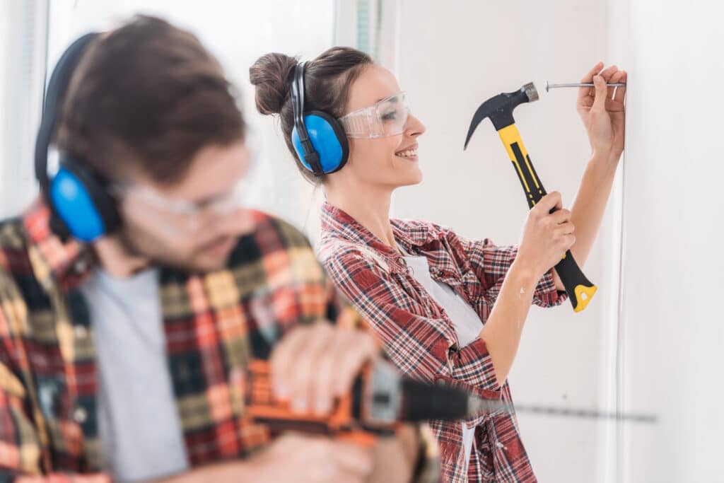 focalisation sélective du jeune couple sur le martelage et le perçage d'un mur pendant pour des travaux de rénovation avec prime CEE