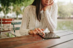 Young woman using digital tablet at outdoor cafe. Female browsing website pages on touch pad while in coffee shop.